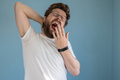Bearded man in glasses and a white t-shirt yawns with mouth wide open, covering it with hand - PhotoDune Item for Sale