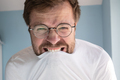 Man with glasses is angry, he tries to contain rage and bites his t-shirt - PhotoDune Item for Sale