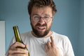 Untidy man points his finger at his unshaven. Caucasian suffers from a hangover, holds a wine bottle - PhotoDune Item for Sale
