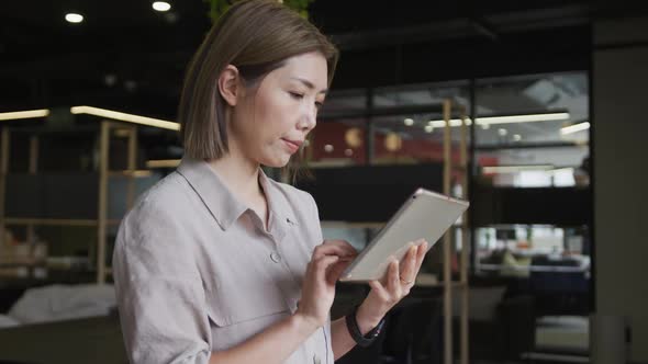 Asian businesswoman standing using a digital tablet in a modern office