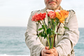 Bouquet of colorful flowers in the hands of mature bearded man in seaside in background. - PhotoDune Item for Sale