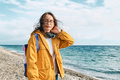 Smiling woman in yellow jacket with  coffee walking along sea coast and enjoying the sunny day.  - PhotoDune Item for Sale