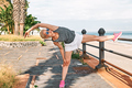 Young beautiful sportive woman training over seaside promenade, stretching legs before jogging. - PhotoDune Item for Sale