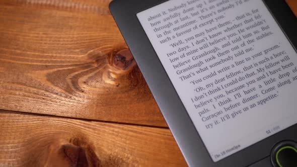 The Electronic Book Lies on a Wooden Table. Screen of Electronic Ink Displays Text of the Book