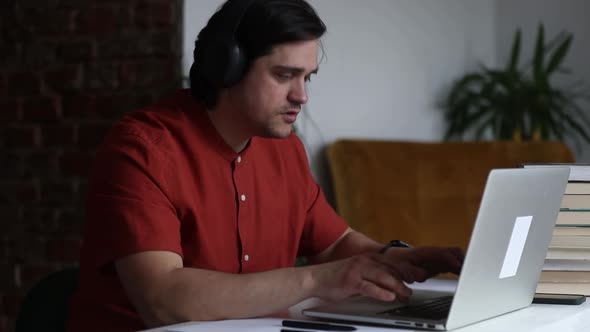 Man working at home office at laptop and talking by web camera