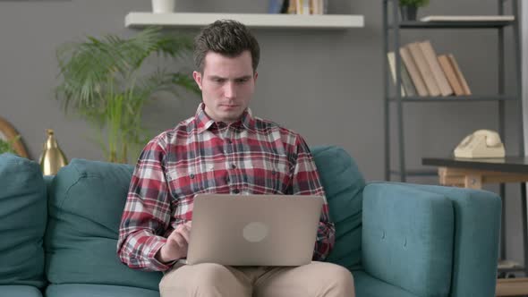 Man with Laptop Reacting to Loss on Sofa