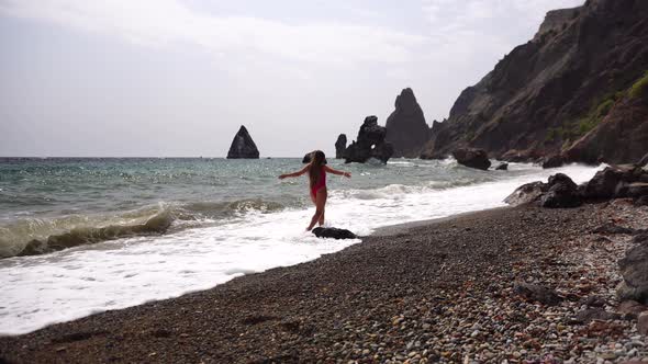 A Young Attractive Brunette Woman with Long Hair in a Red Swimsuit and Santa Hat Walks Along the