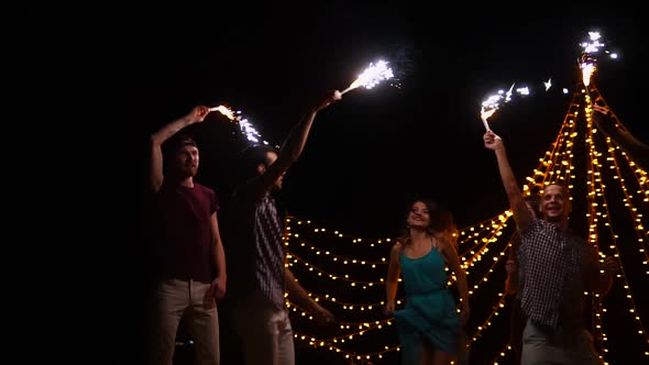 Company of Happy Friends Dancing at Night with Bright Torches in Hands