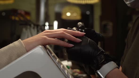 Closeup Side View of Unrecognizable Manicurist Master in Black Gloves Removing Gel Polish From Nails