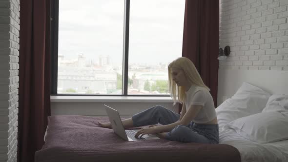 Young Woman Works at a Laptop in a Cozy Bright Bedroom