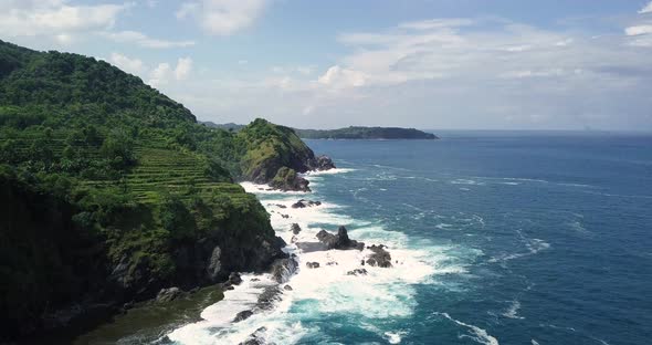Slow forward flight along coastline of Siung Beach and agricultural plantation growing on hill