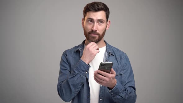 Portrait of cheerful brunette man with beard using cellphone and smiling, reading good news