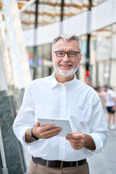 Older senior professional business man using digital tablet standing outdoors.