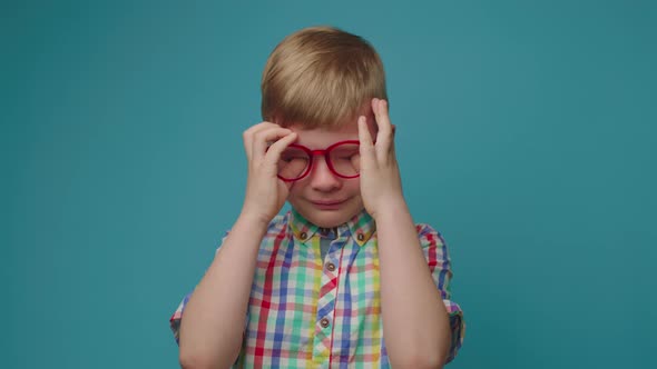 Exhausted Upset Crying Preschool Boy in Eye Glasses Wiping Tears Away with Hands Standing on Blue