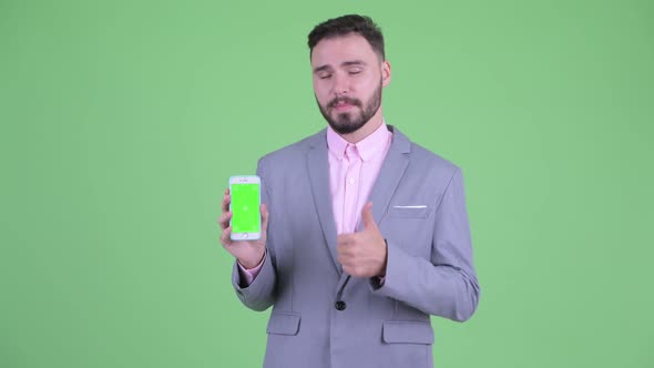 Happy Young Bearded Businessman Showing Phone and Giving Thumbs Up