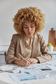 Serious female entrepreneur dressed in formal brown jacket writes down notes does paper work poses - PhotoDune Item for Sale