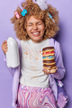 Vertical shot of curly haired woman poses with tummy anticipates for baby holds pile of delicious - PhotoDune Item for Sale