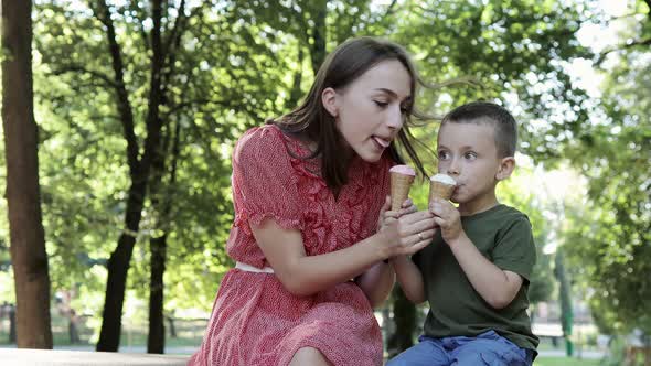 Smiling young mother and little son eating ice-creams together in a summer park