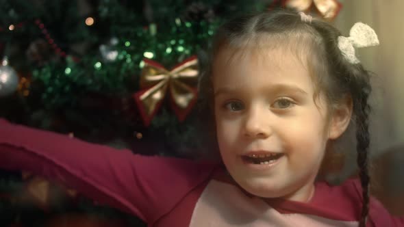 Happy Little Girl Singing a Christmas Song on the Background of Christmas Tree