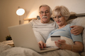 Happy senior couple shopping on the Internet while using laptop in bedroom. - PhotoDune Item for Sale