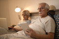 Senior man surfing the net on touchpad in bed at night. - PhotoDune Item for Sale