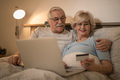 Happy mature couple using credit card and laptop while resting in bedroom. - PhotoDune Item for Sale