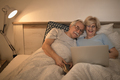 Happy senior couple surfing the net on laptop in bedroom at night. - PhotoDune Item for Sale