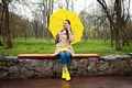 Happy senior woman in yellow rain coat with yellow umbrella is talking on a smartphone and walking - PhotoDune Item for Sale