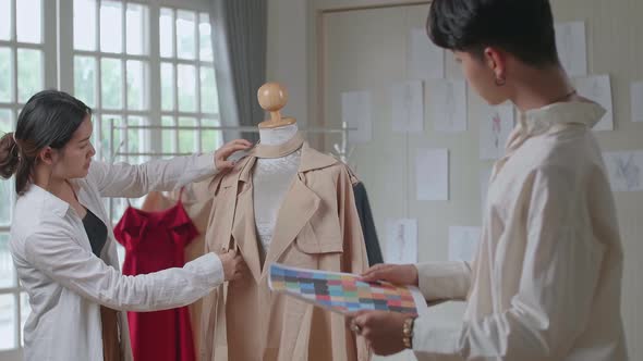 Two Young Asian Fashion Designers Check Color Of Clothes On Mannequin Model