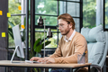 Young serious thinking businessman at work inside office with computer, blond man in casual clothes - PhotoDune Item for Sale
