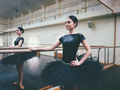 Ballerina in black tutu dress stretches on barre in ballet gym. Standing mirror - PhotoDune Item for Sale