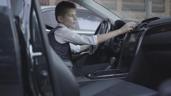 Cute Little Boy in Business Suit Sitting in the Car Studying the Salon