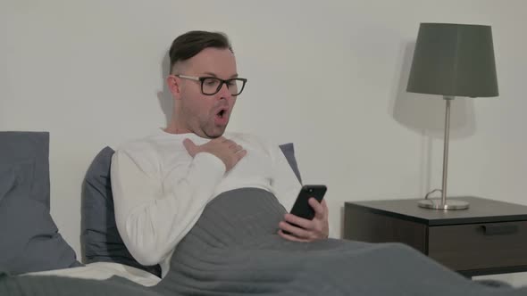 Casual Man Reacting to Loss on Smartphone in Bed