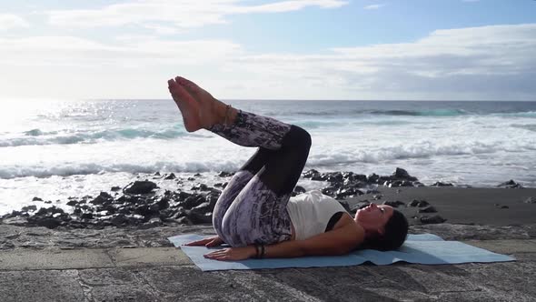 Woman in Sport Clothes Practicing Yoga and Meditating on Beach in Morning