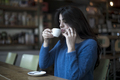 Beautiful female is drinking delicious coffee while sitting in the bar while talking by phone - PhotoDune Item for Sale