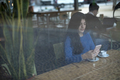 Smiling woman in cafe using mobile phone and texting in social networks, sitting alone - PhotoDune Item for Sale