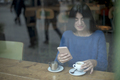 Smiling woman in cafe using mobile phone and texting in social networks, sitting alone - PhotoDune Item for Sale