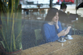 Smiling woman in cafe using mobile phone and texting in social networks, sitting alone - PhotoDune Item for Sale