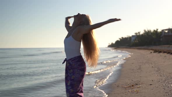 Pretty mature woman on a beach raises her arms and turns around with emotion of freedom.