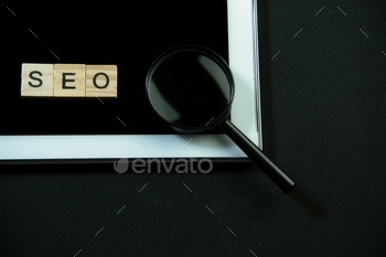 SEO written in wooden letters, tablet and a magnifying glass.