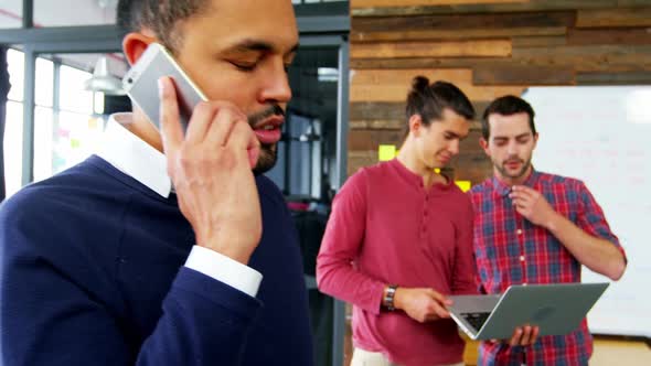 Business executive talking on mobile phone while colleague working in background