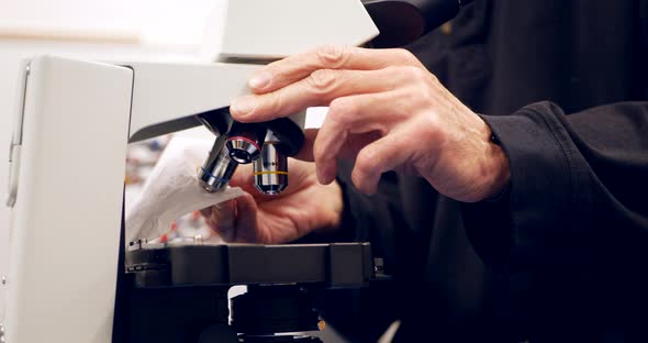 A college professor cleaning the lens of a microscope to show his students in a biology research lab