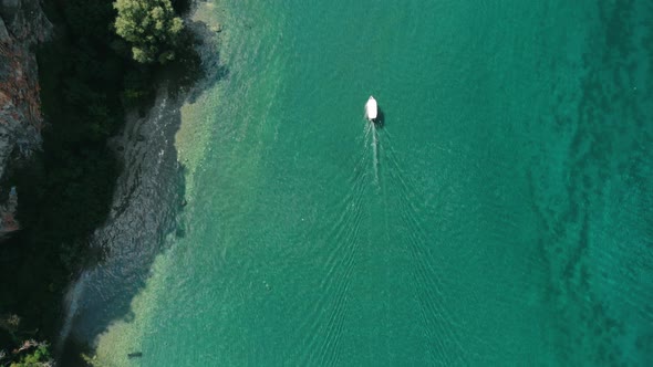 Aerial (drone) shot of a boat slowly moving on turquoise water of Ohrid Lake along wild Macedonian c