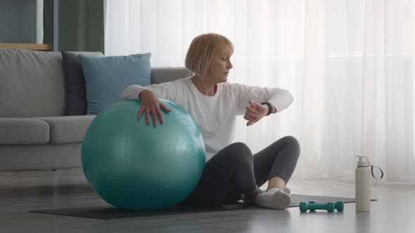 Senior Female Using Fitness Tracker After Training With Fitball Indoors