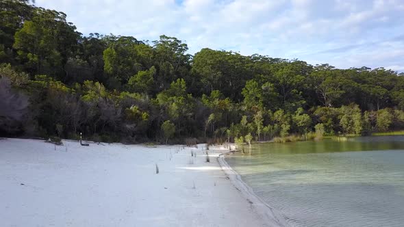 Drone footage flying backwards revealing a beautiful isolated white sandy beach. Located Lake McKenz