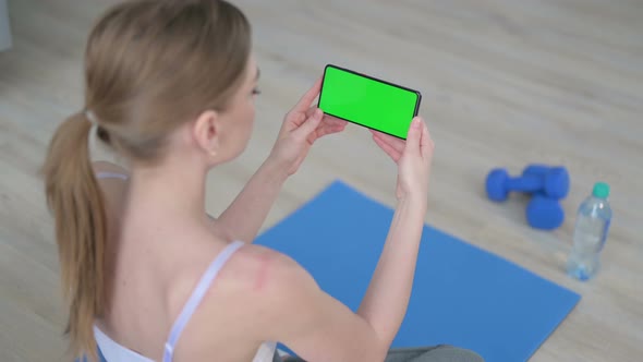 Rear View of Young Woman Looking at Smartphone with Chroma Key Screen on Yoga Mat