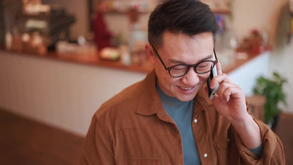 Laughing Asian young man wearing eyeglasses talking on phone