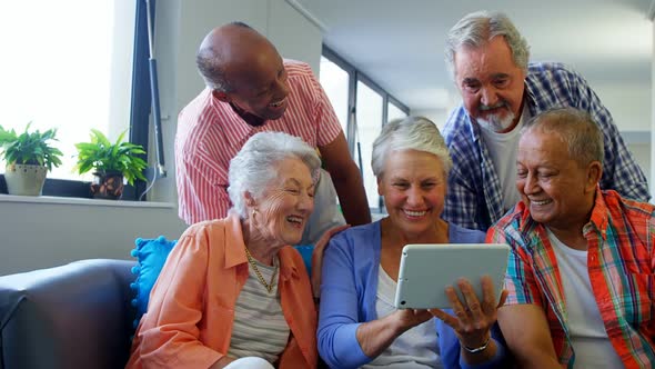 Happy senior friends using digital tablet on sofa