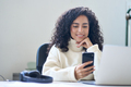 Young smiling latin business woman using phone in office sitting at desk. - PhotoDune Item for Sale