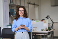 Happy young business woman holding phone standing in office using mobile. - PhotoDune Item for Sale